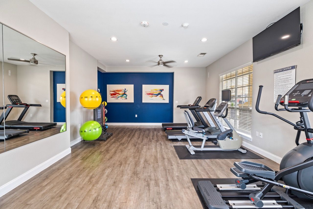 Bright on-site fitness center with treadmills, ellipticals, a stationary bike, and weights.
