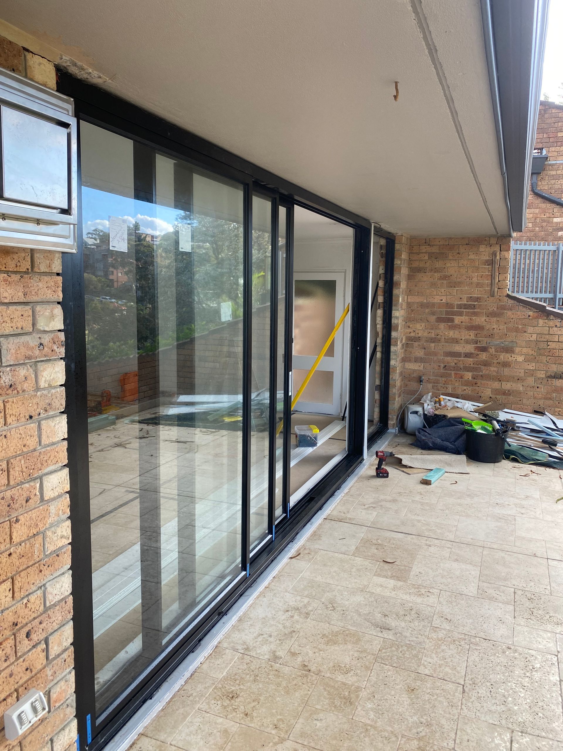 Covered patio with sliding glass doors, brick wall, and construction items on the ground — Kracken Windows and Doors In Terrey Hills, NSW