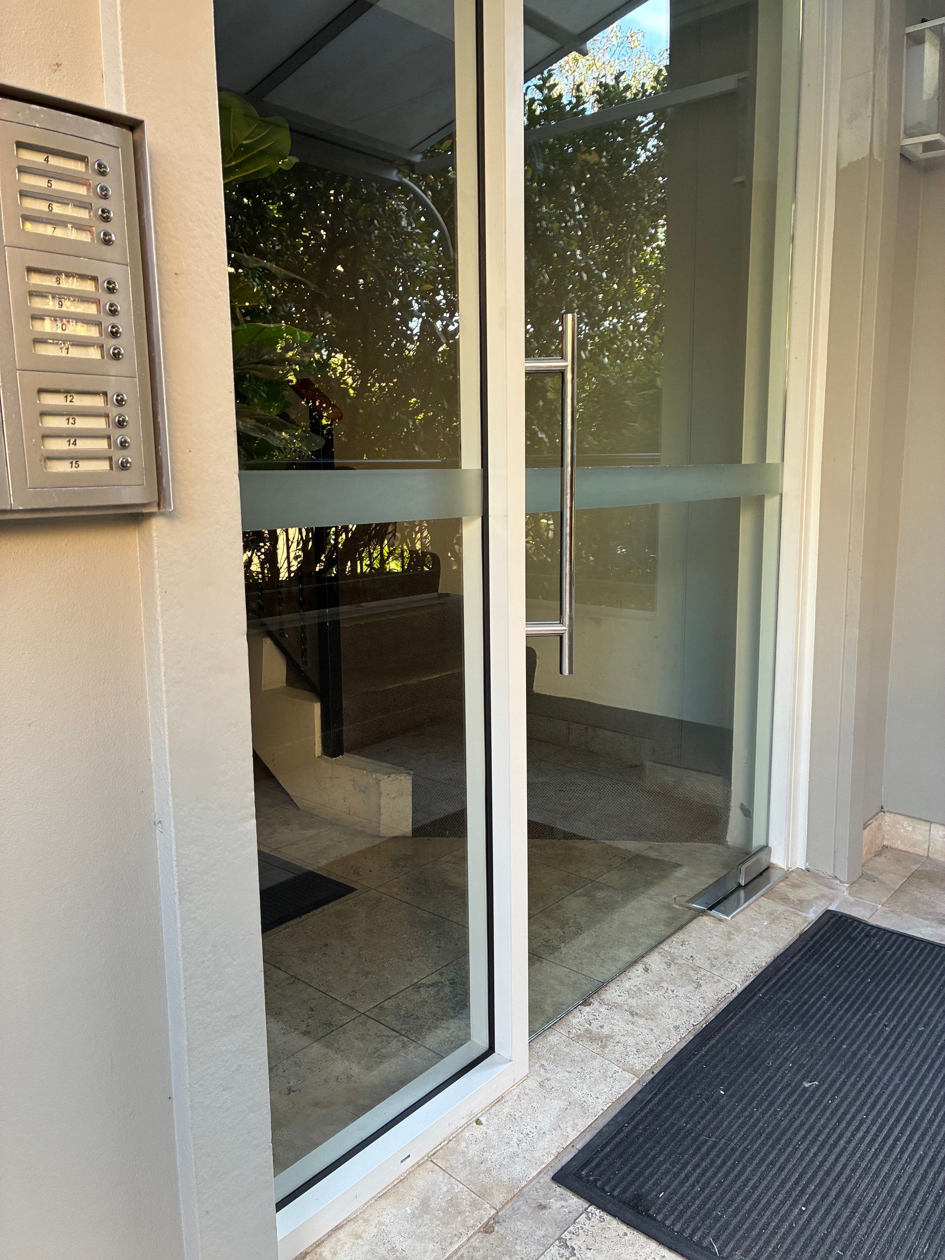 Front entrance with glass door, stone steps, and black doormat by a beige wall. — Kracken Windows and Doors In Terrey Hills, NSW