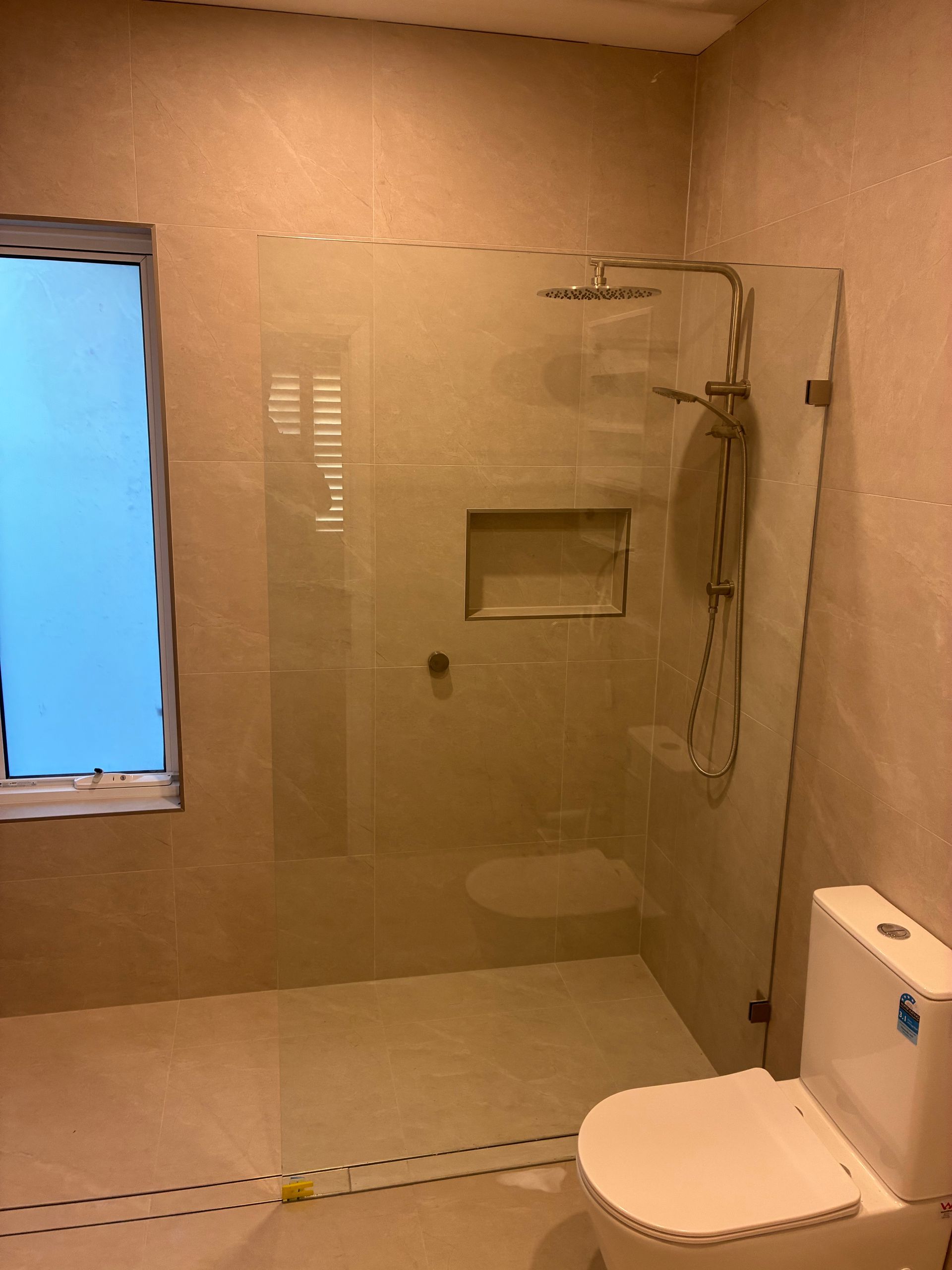 Bathroom with walk-in shower, handheld showerhead, wall niche, and a toilet beside a blue window. — Kracken Windows and Doors In Terrey Hills, NSW