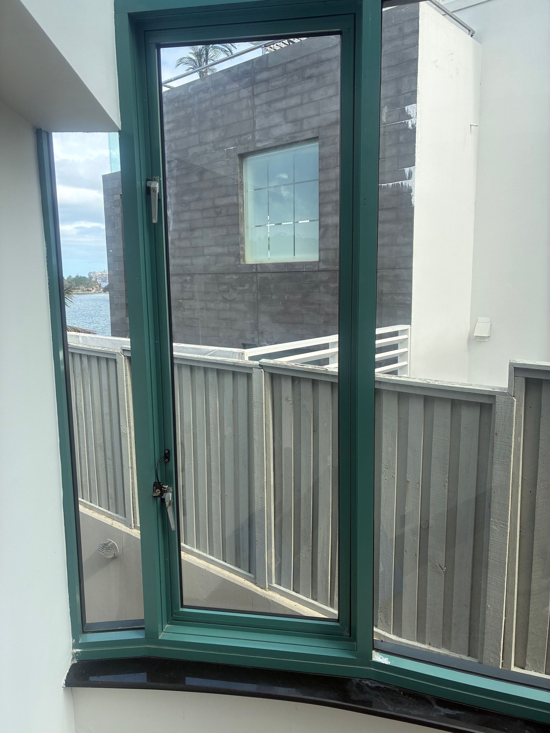 Balcony view through a green-framed window toward neighboring buildings and a wooden fence with snow on top — Kracken Windows and Doors In Terrey Hills, NSW