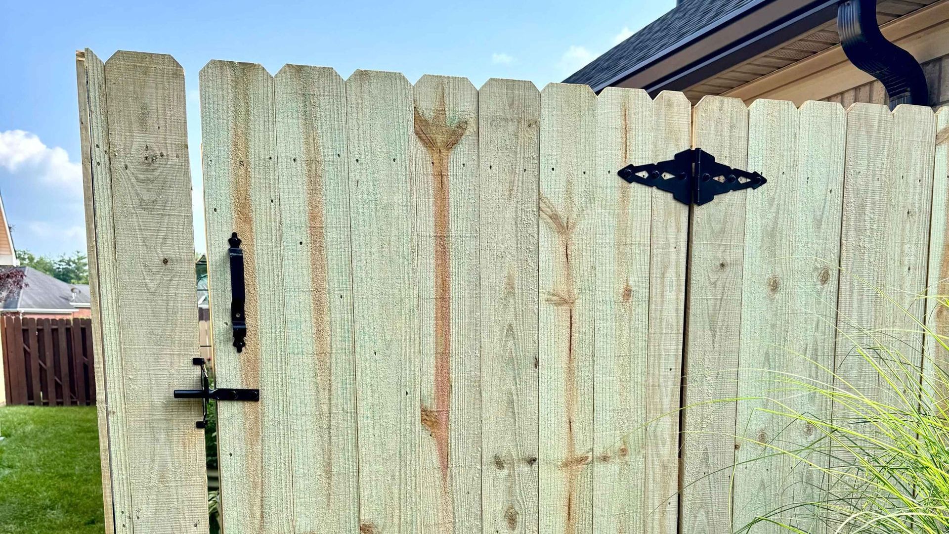 A close up of a wooden fence with a gate and a house in the background.