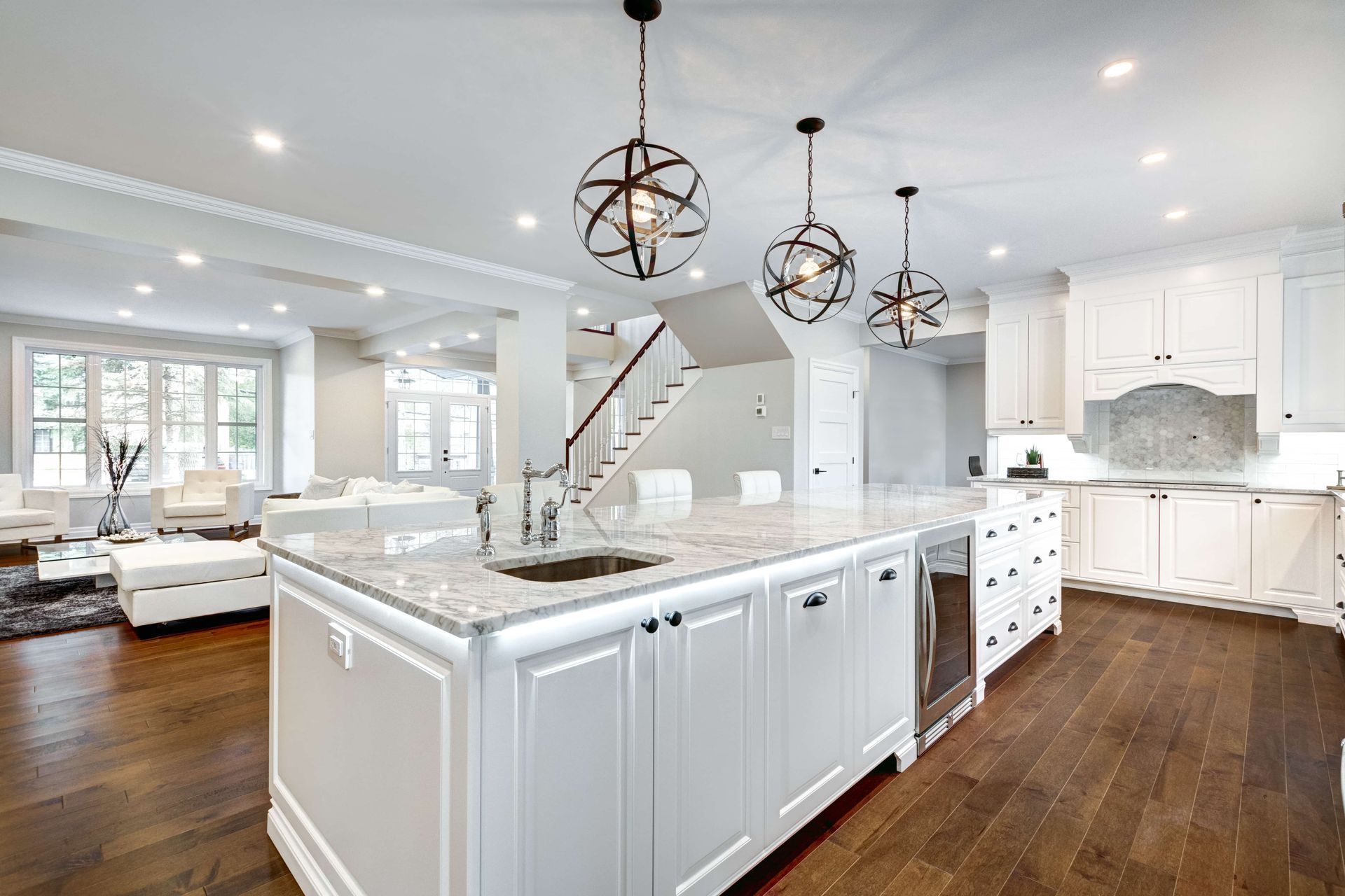 Spacious, white kitchen with a large island, dark wood floors, and hanging globe lights.