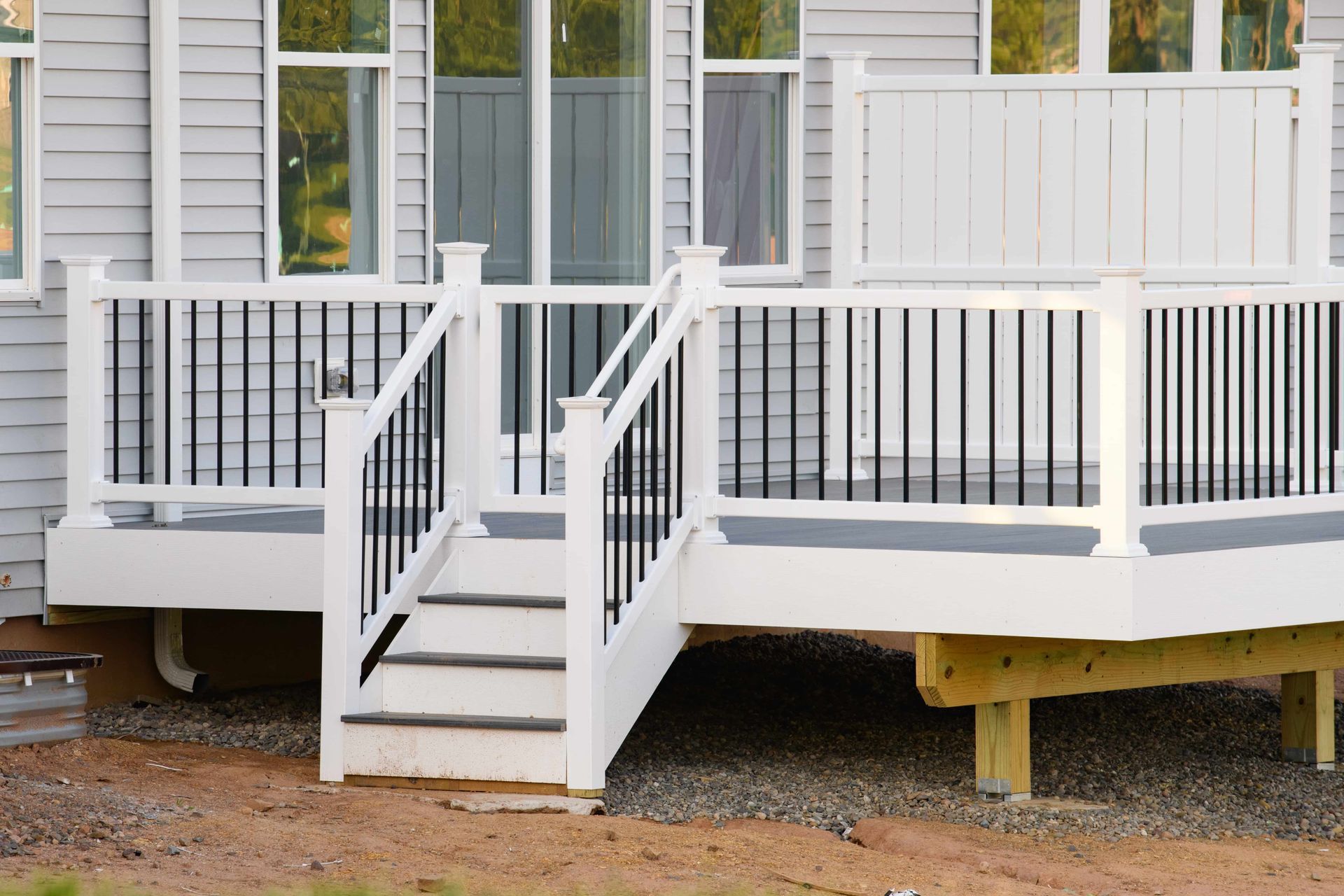 White deck with black railings, steps, and a house in the background.