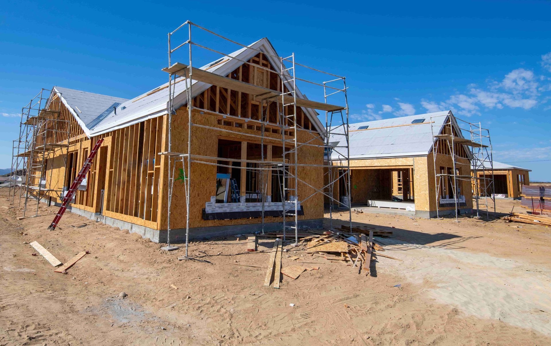 Houses under construction with exposed wooden frames against a clear blue sky.