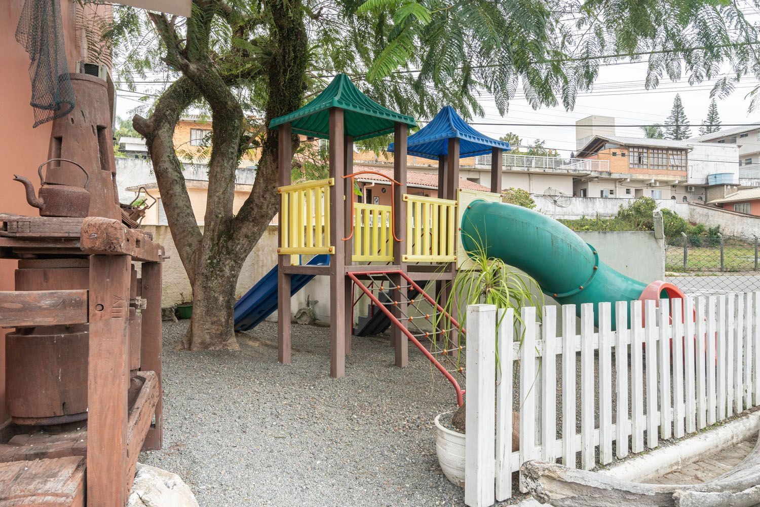 Há um playground com um escorregador e uma árvore ao fundo.