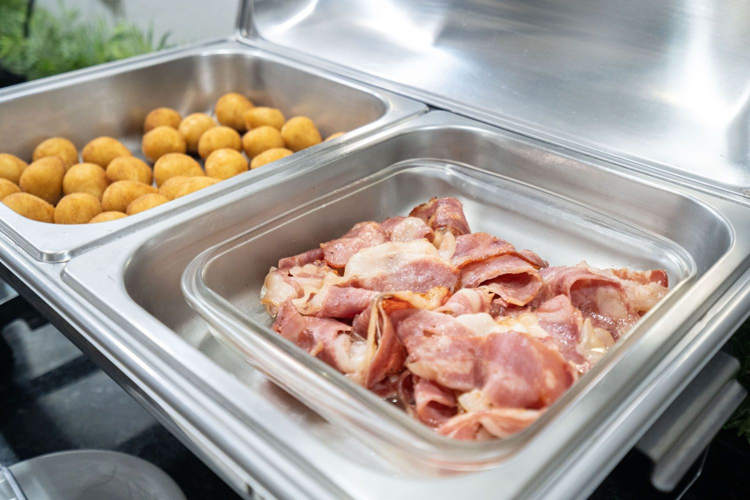 Há duas bandejas de comida em um bufê, uma das quais é bacon.