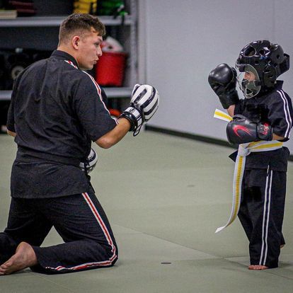 A man is kneeling down next to a young boy wearing boxing gloves.
