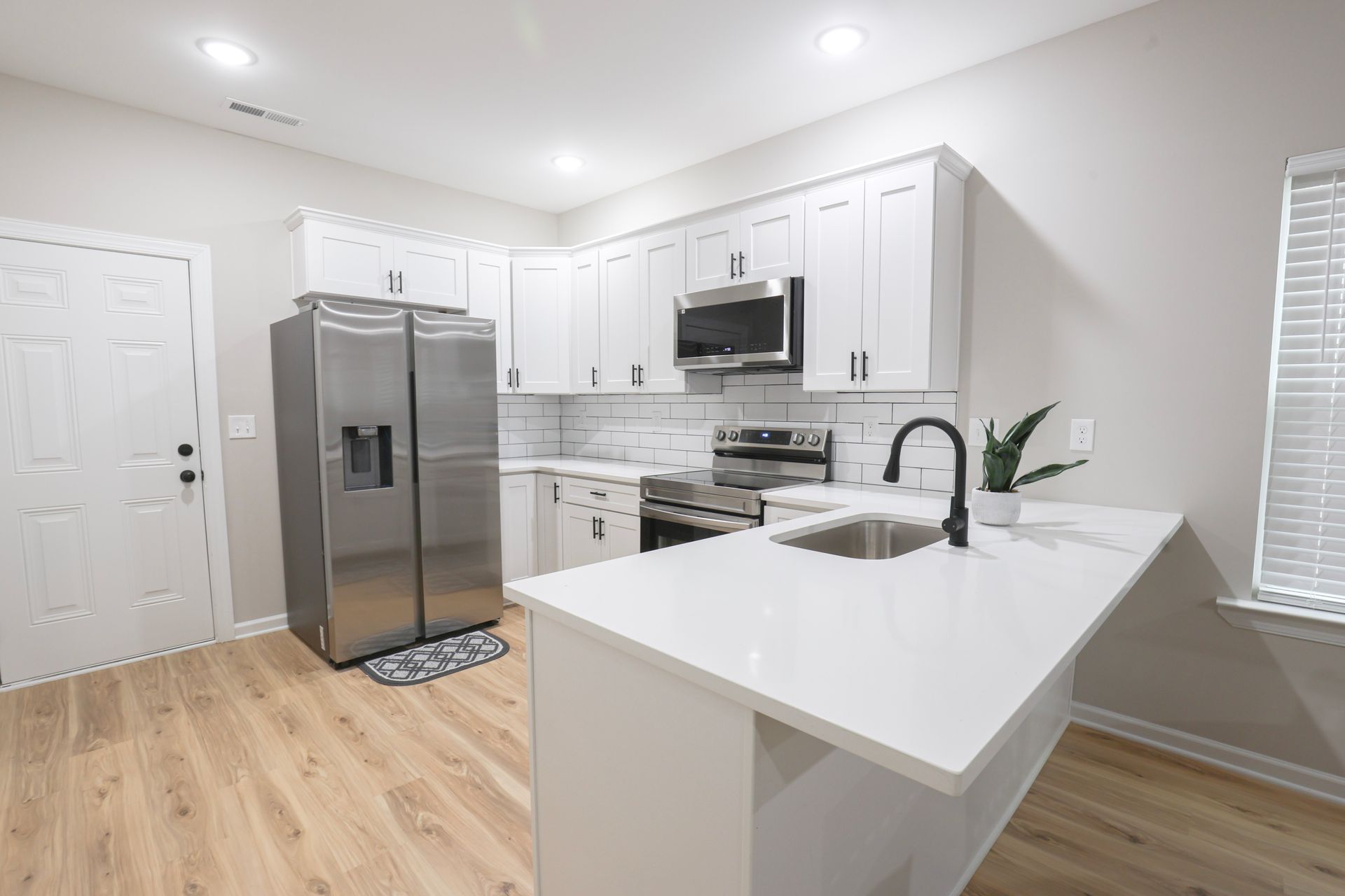 Modern kitchen with white cabinets, stainless steel appliances, and a white countertop island. | Next Level Family Solutions