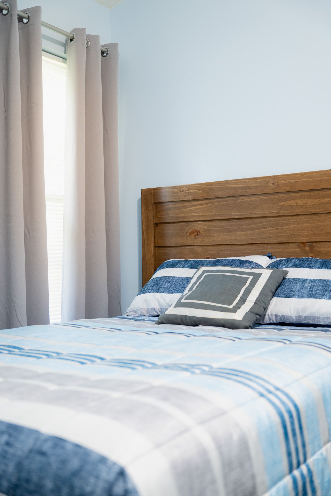 Bedroom with a wooden headboard, striped blue and gray bedding, and a decorative pillow.