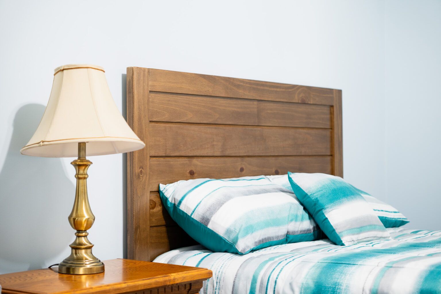 Wooden bed headboard, turquoise bed linens, nightstand with lamp.