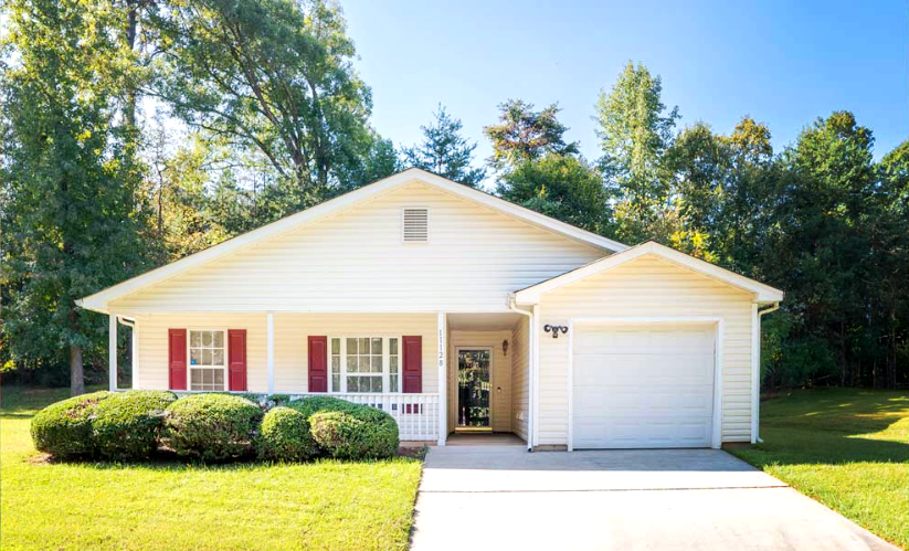 White house with red shutters and a single-car garage, set on a green lawn with a clear sky. | Next Level Family Solutions
