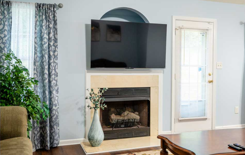 Living room with fireplace, TV, and door to outside; light blue walls, brown flooring, and patterned curtains.
