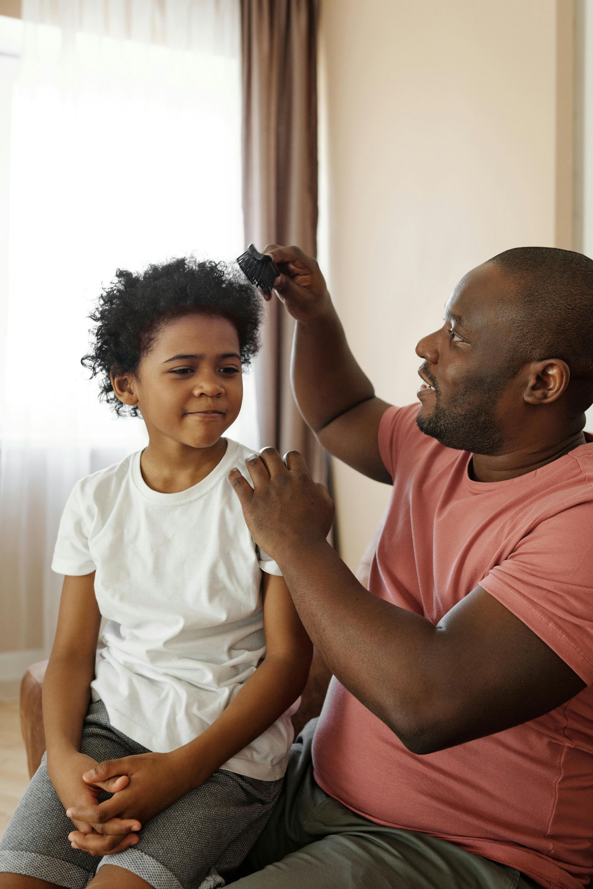 Man combing child's hair indoors; child looking at the camera.