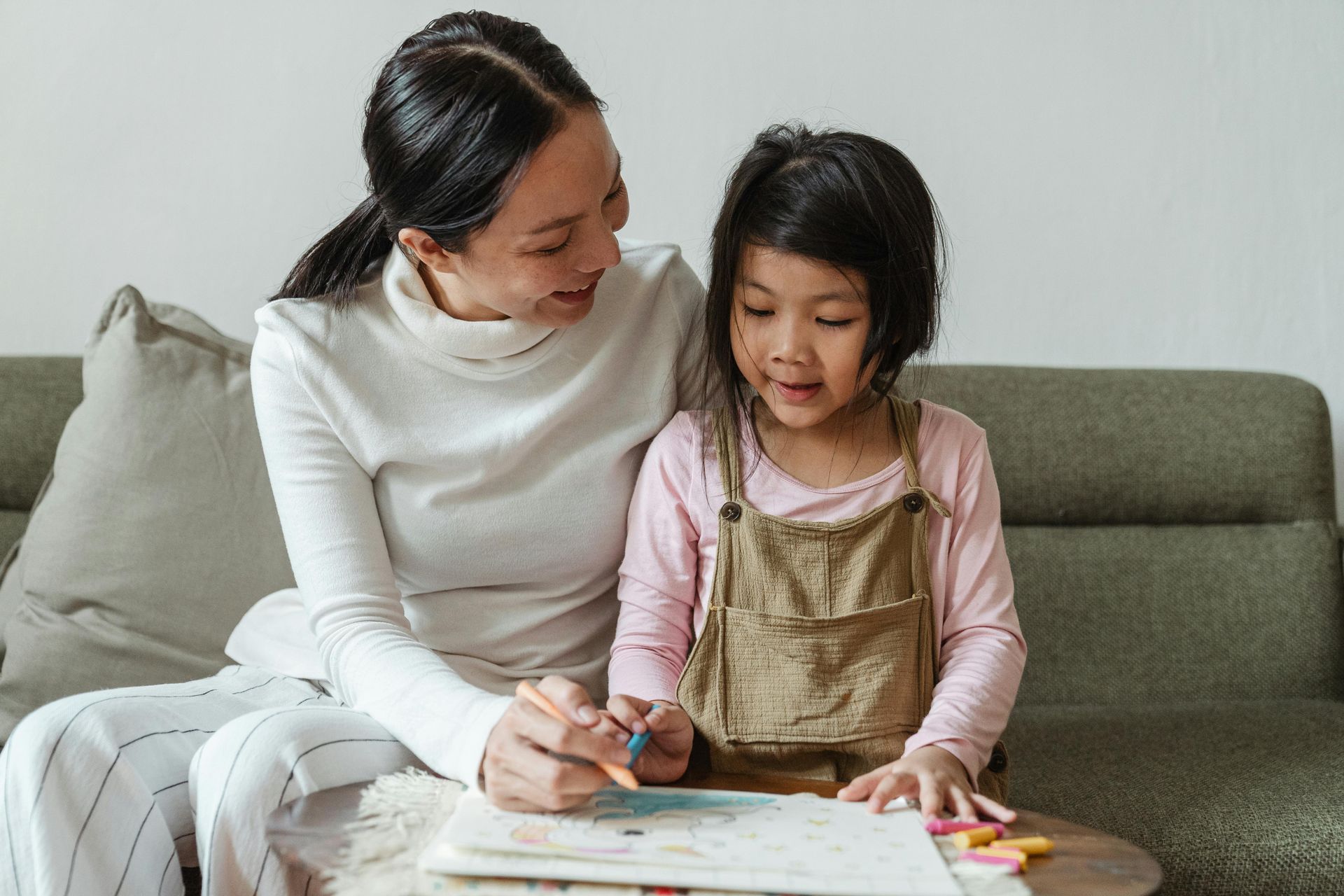 Woman and child drawing together on a small table on a sofa.