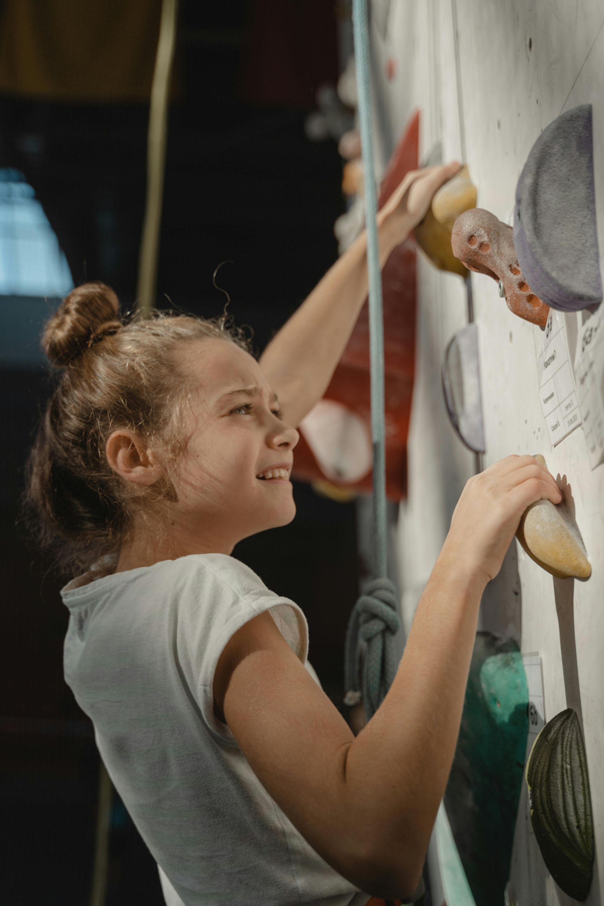 Young person climbing a colorful indoor rock wall, smiling, holding onto handholds.