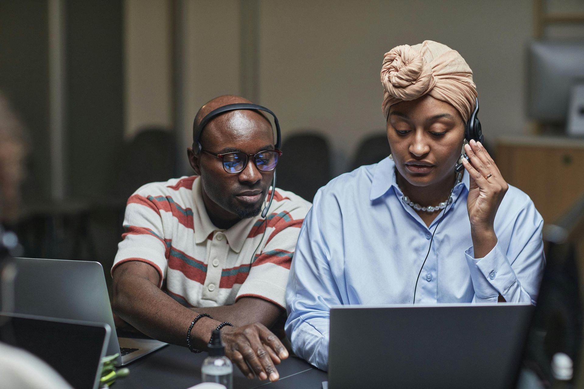 Two people wearing headsets, working on laptops in an office.