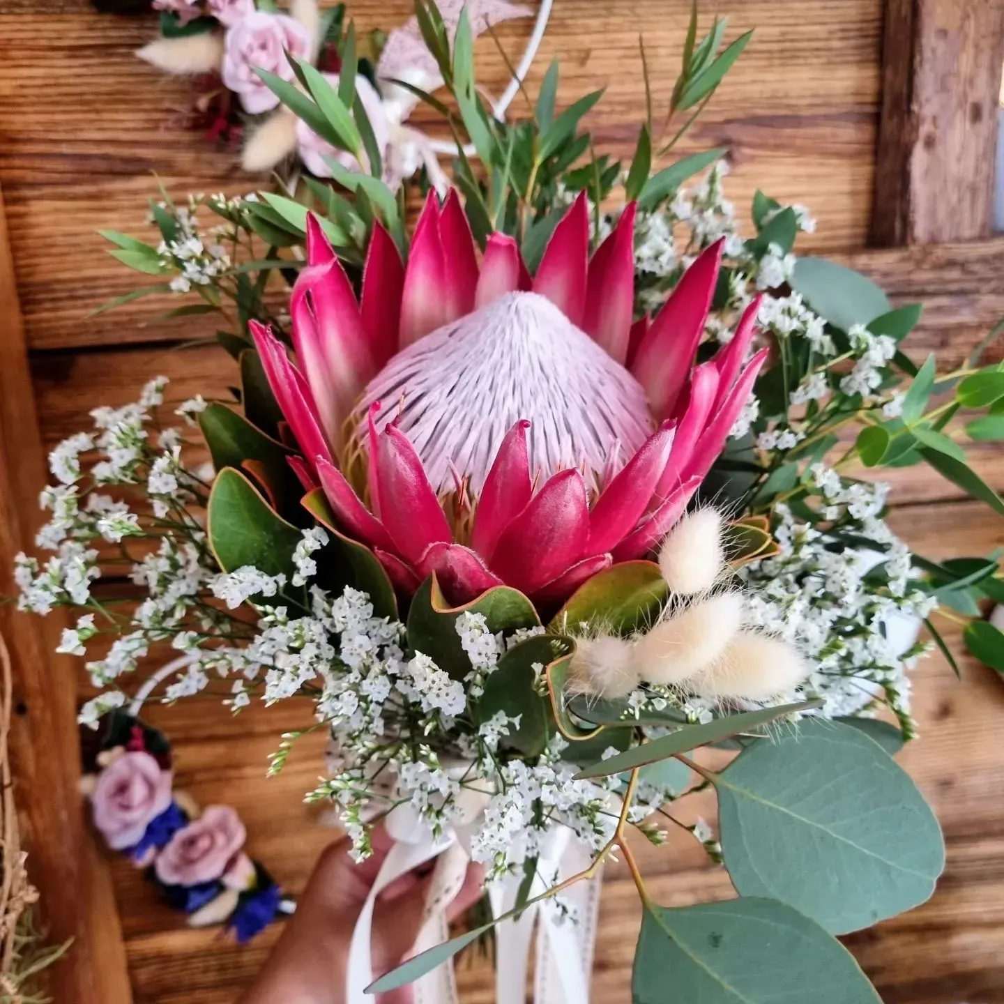 Una persona tiene in mano un mazzo di fiori davanti a una parete di legno.