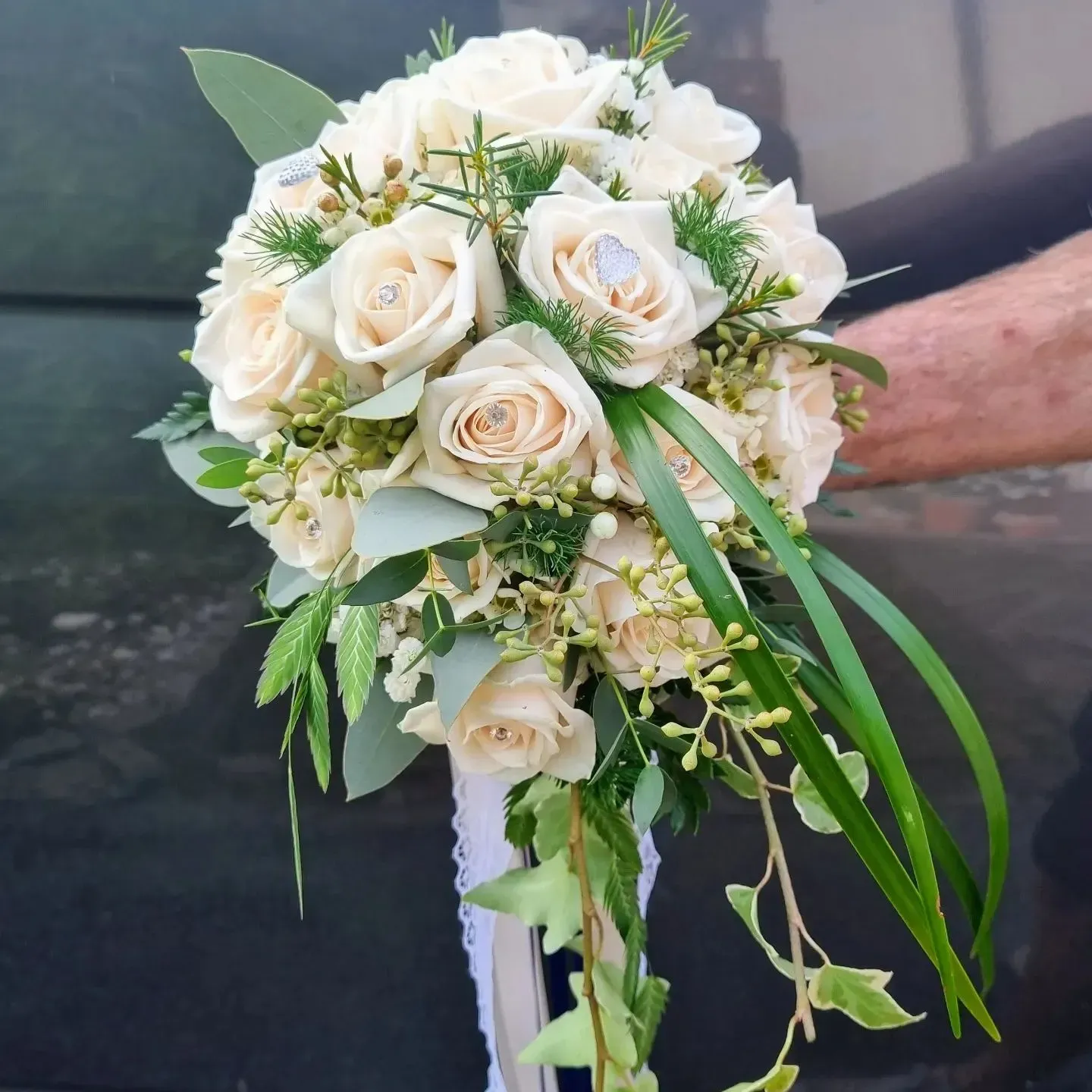 Una persona tiene in mano un mazzo di rose bianche e piante verdi
