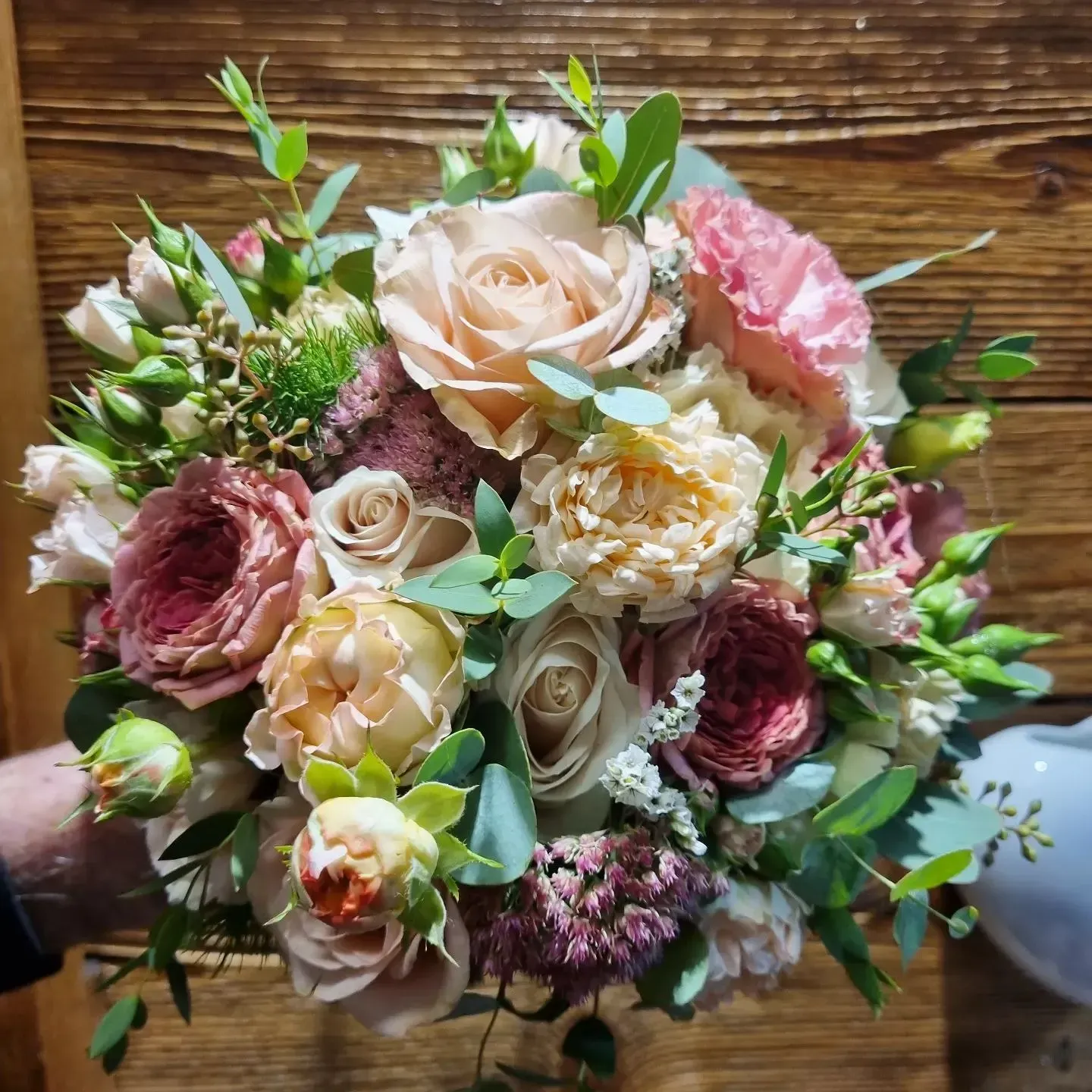 Una persona tiene in mano un mazzo di fiori davanti a una parete di legno