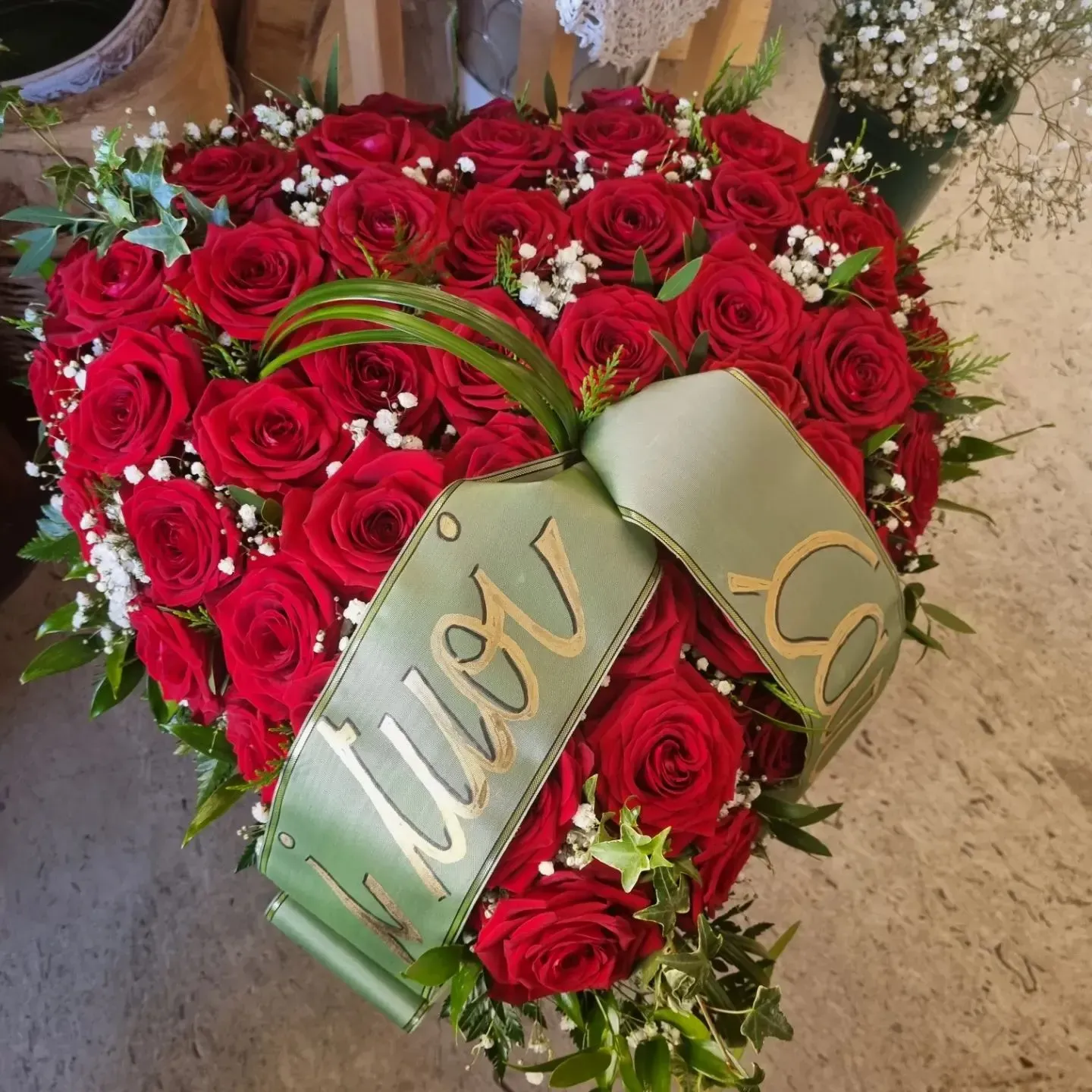 Una composizione a forma di cuore di rose rosse con un nastro verde con la scritta