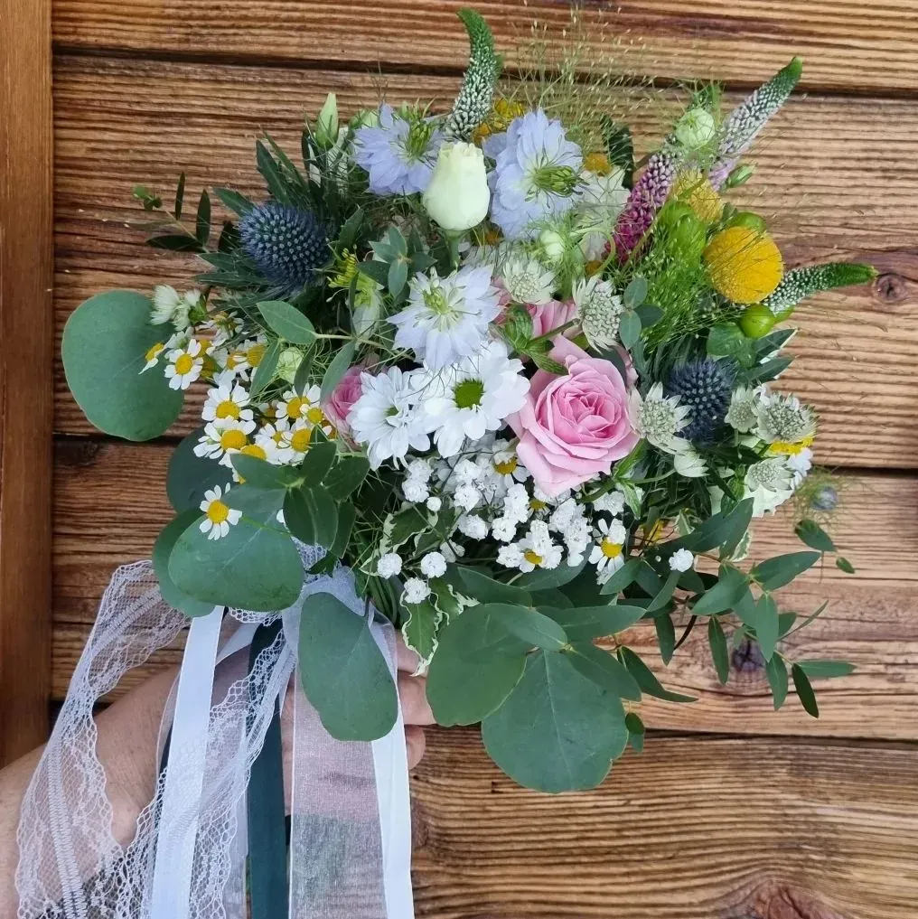 Una persona tiene in mano un mazzo di fiori davanti a una parete di legno.