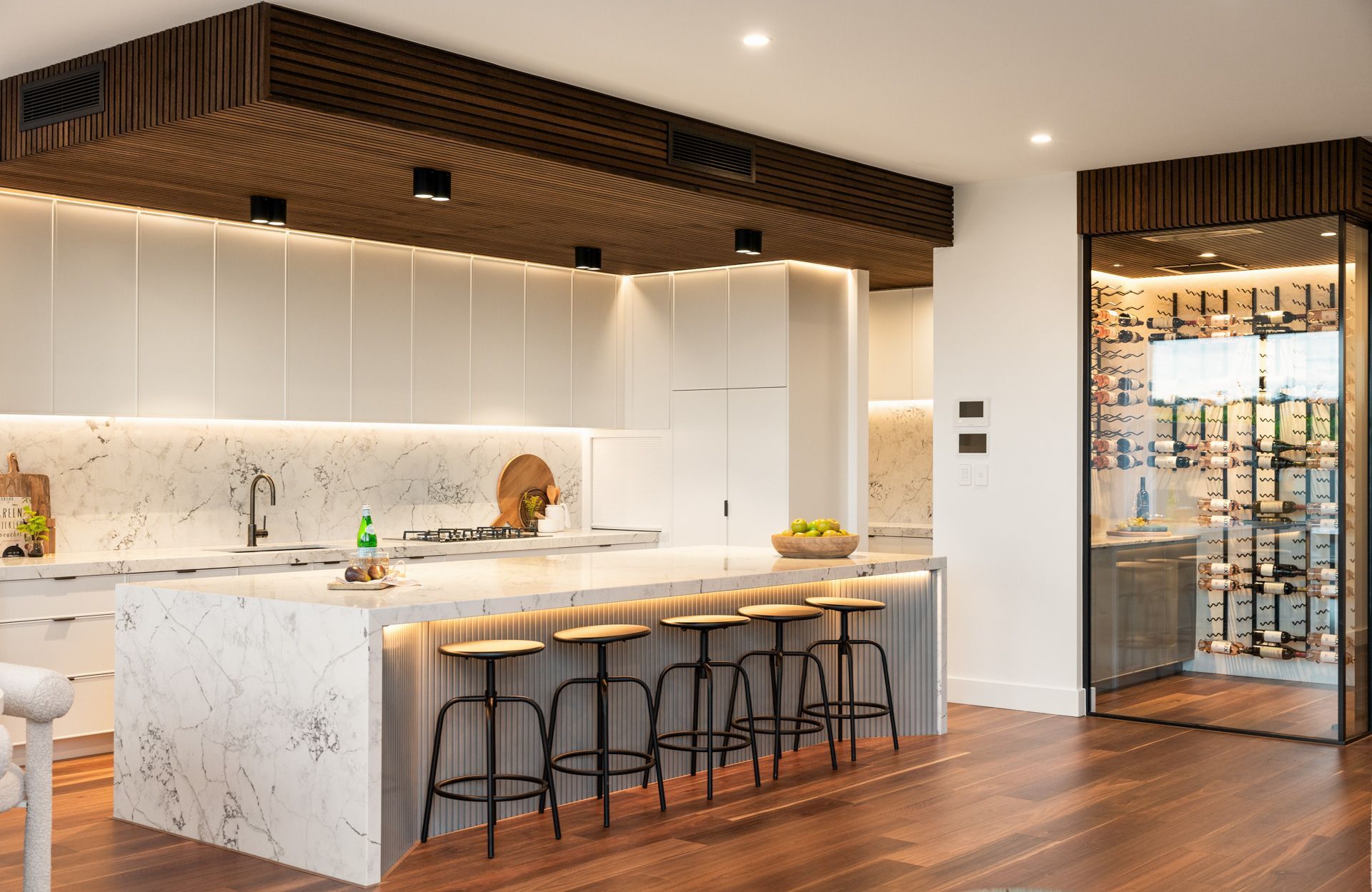 Modern kitchen with marble countertops and island, wooden accents, and a glass-enclosed wine cellar.