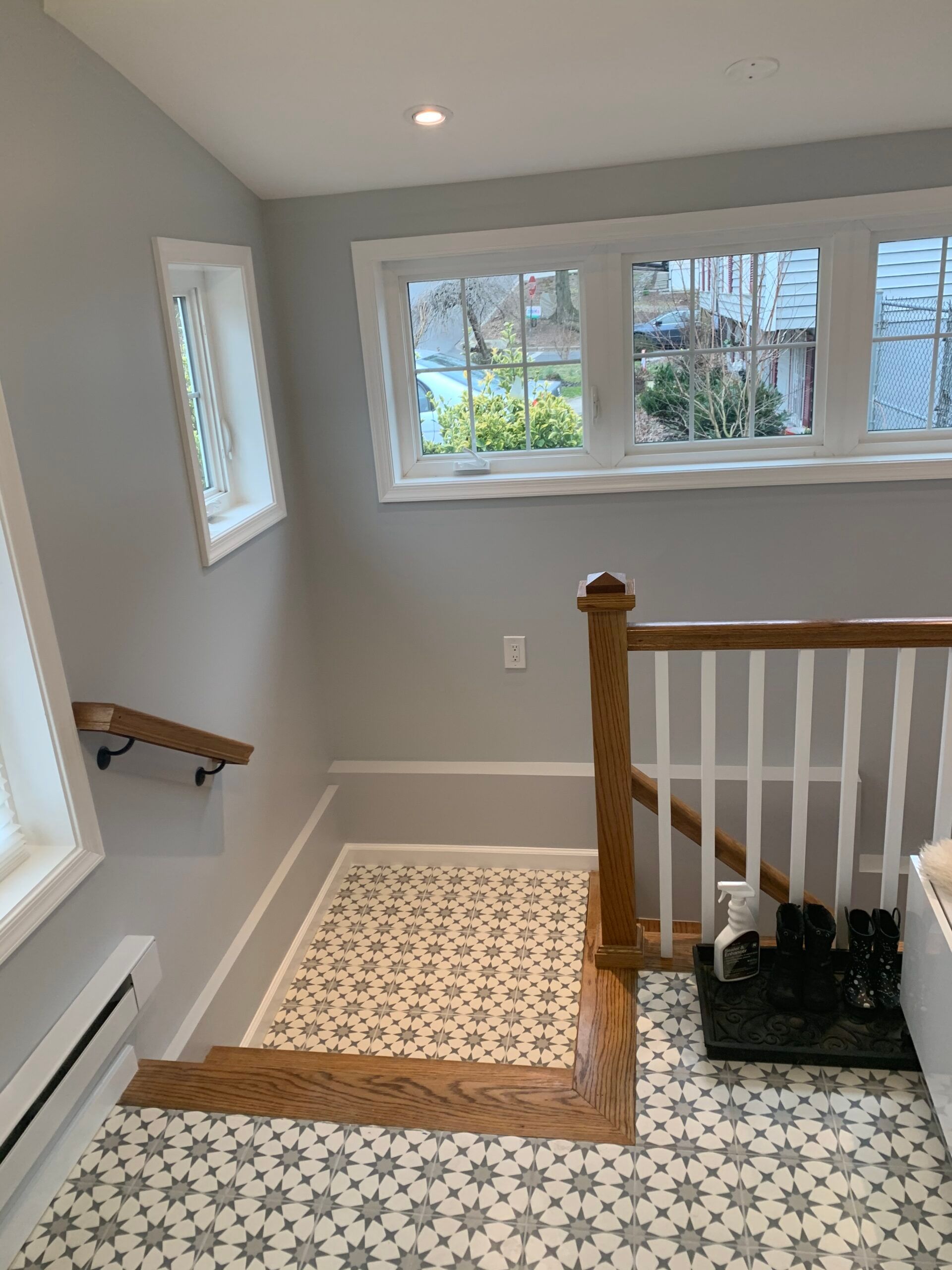 Staircase with patterned floor tiles, wood handrails, and white walls. Light grey paint and a window.