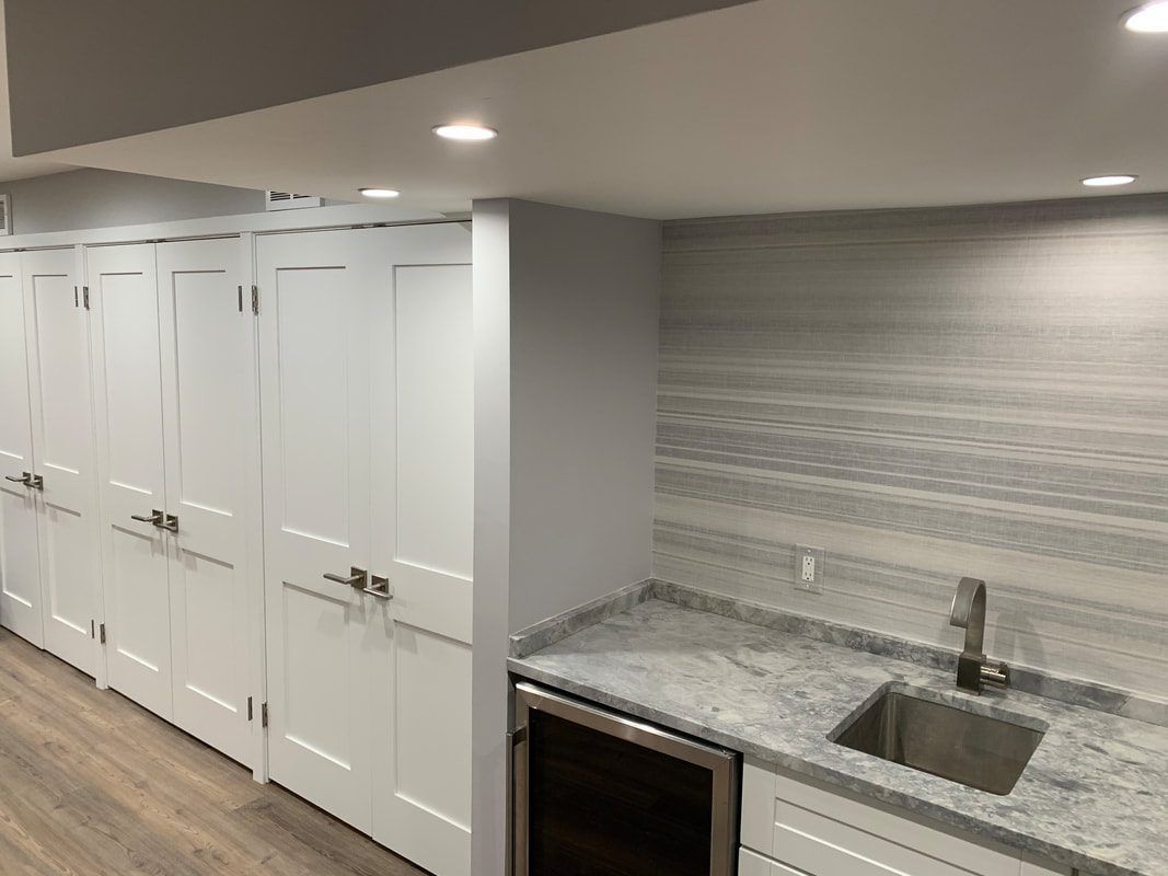 A white kitchen cabinet and countertop with a sink, wine fridge, and backsplash.