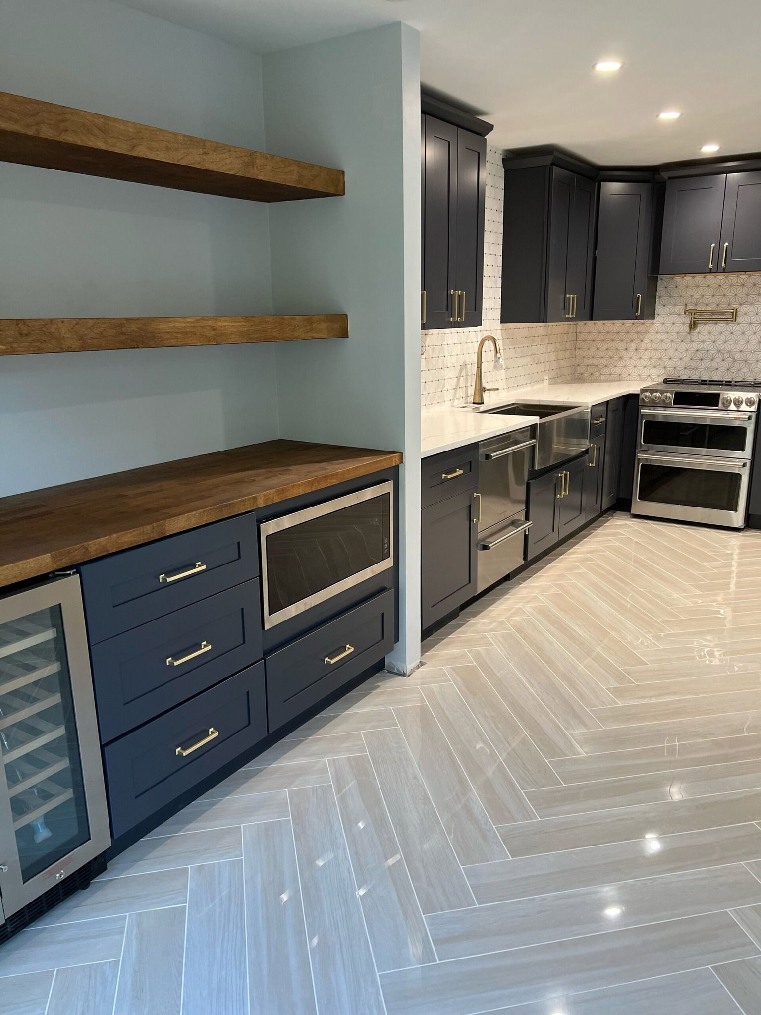 Kitchen renovation with dark blue cabinets, wood shelves, stainless steel appliances, and light gray flooring.