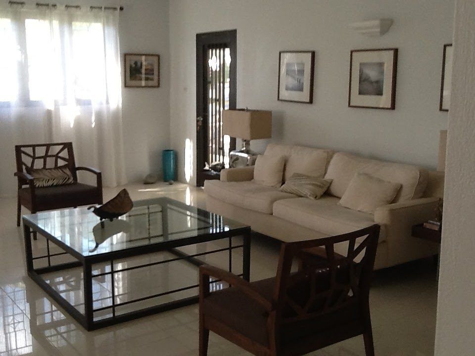 Living room with cream couch, dark chairs, glass coffee table, and framed art.