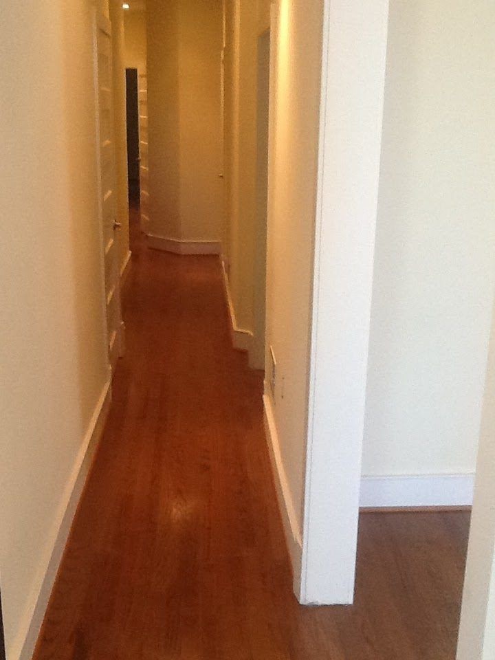 Hallway with hardwood floors and white walls, leading to a doorway.