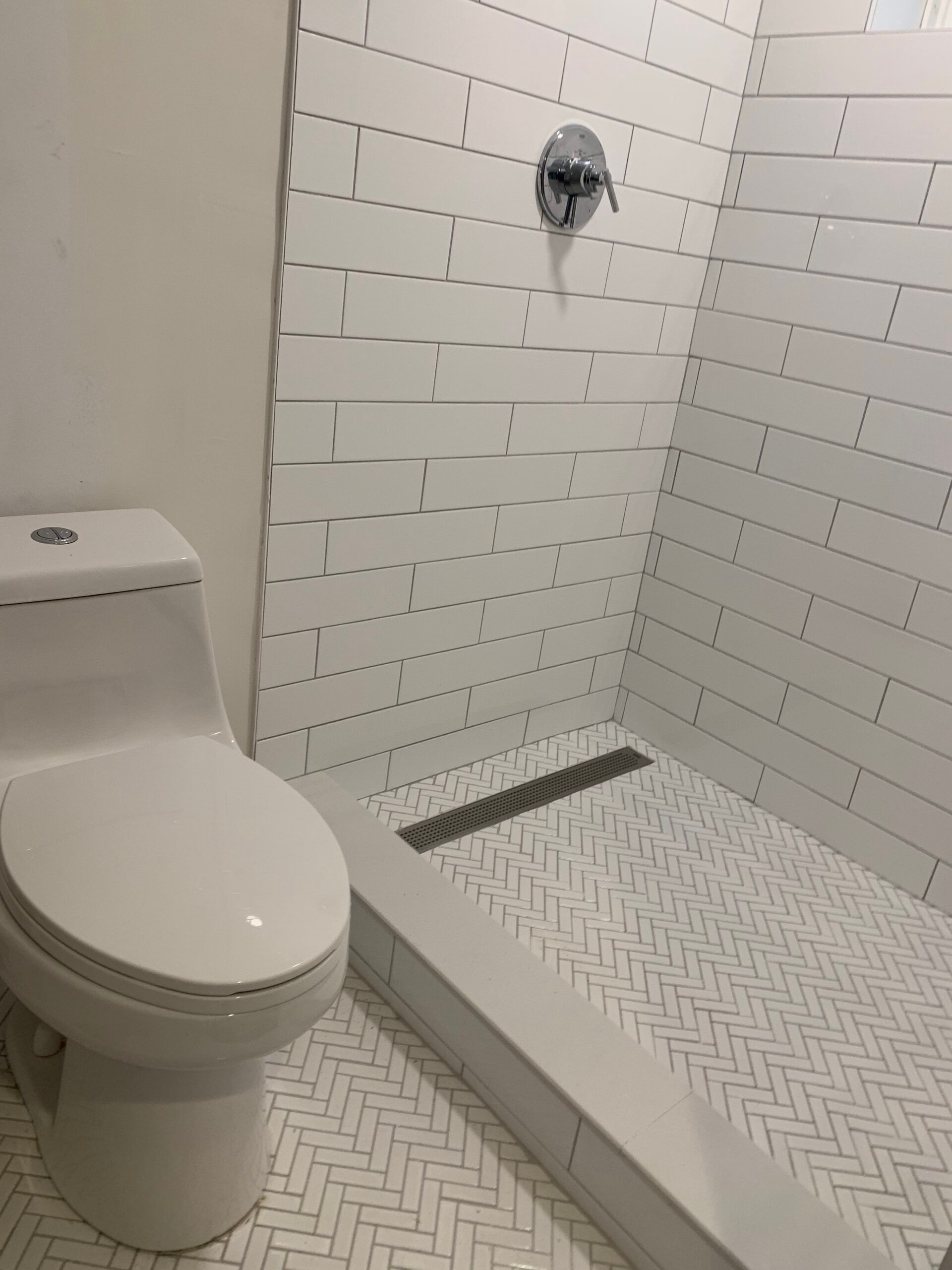 White tiled bathroom with toilet, shower, and drain.