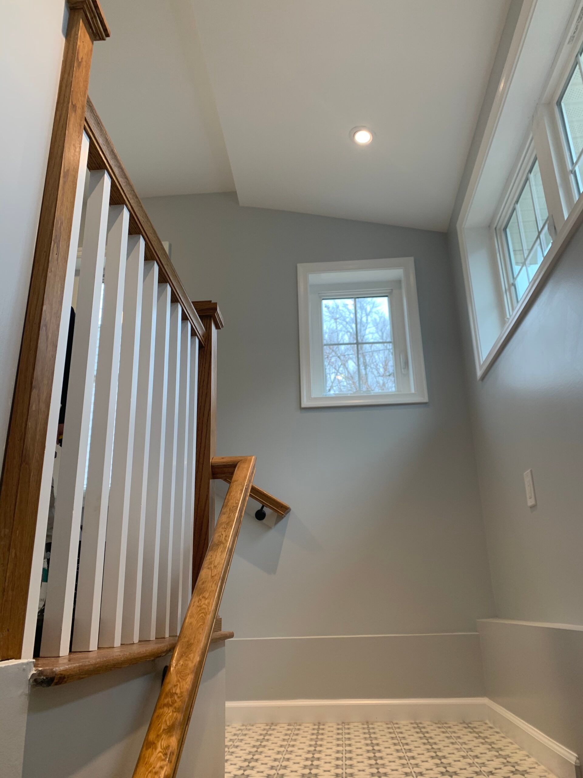 Staircase with wooden handrail, white balusters, light gray walls, and a small window.