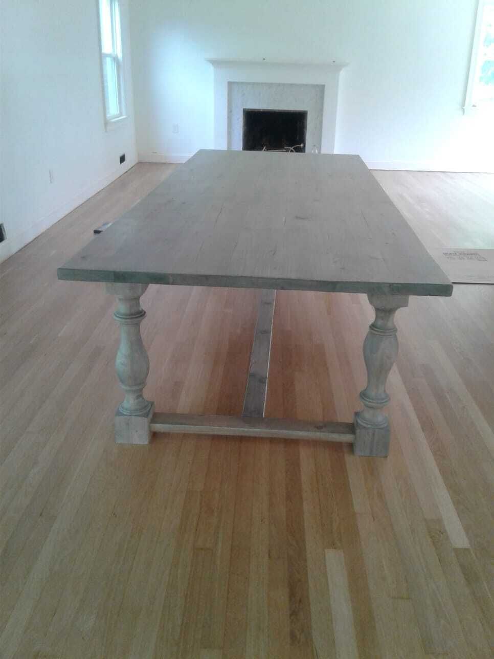 A large wooden table with turned legs in a light-colored room with a fireplace and wood floor.