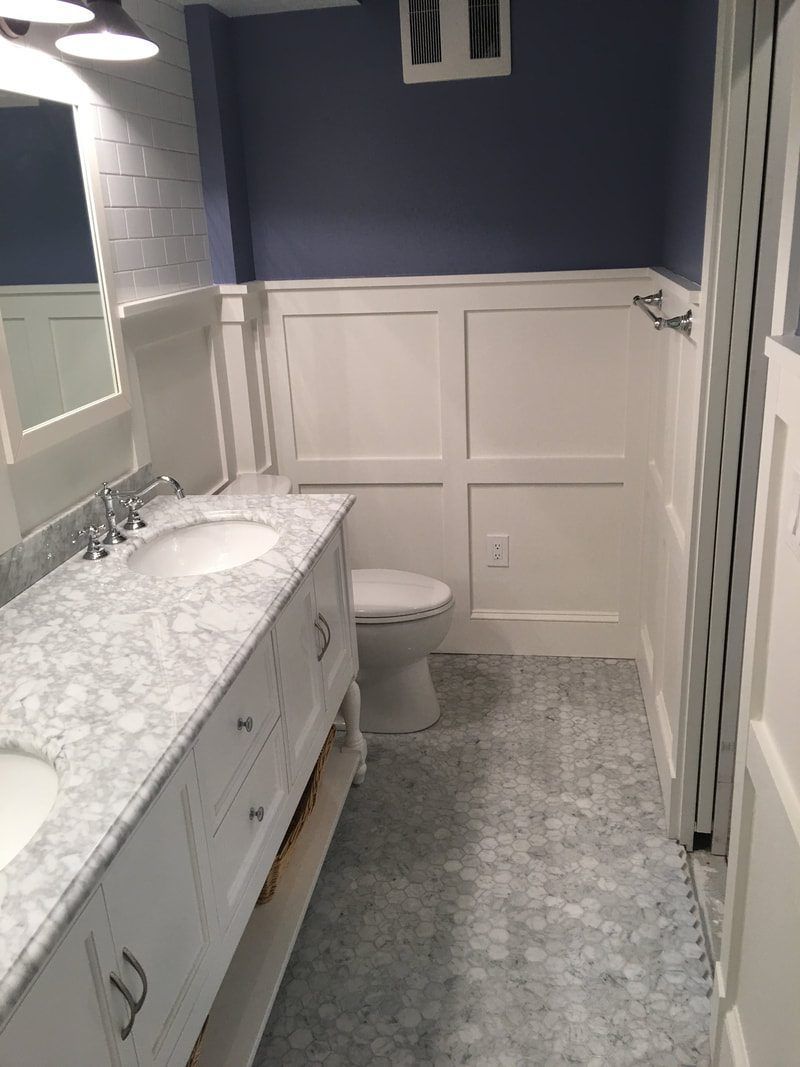 Bathroom with white vanity, marble countertop, white wainscoting, blue wall, and gray tile floor.