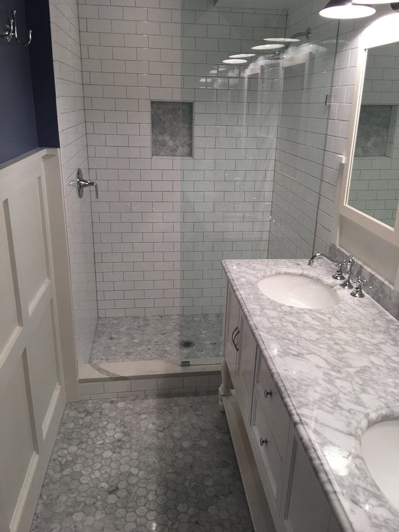 Bathroom with white subway tile shower, marble vanity, and blue wall.