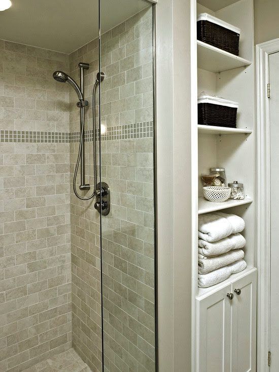 Shower with tiled walls and glass door, adjacent built-in white storage shelves holding baskets and towels.