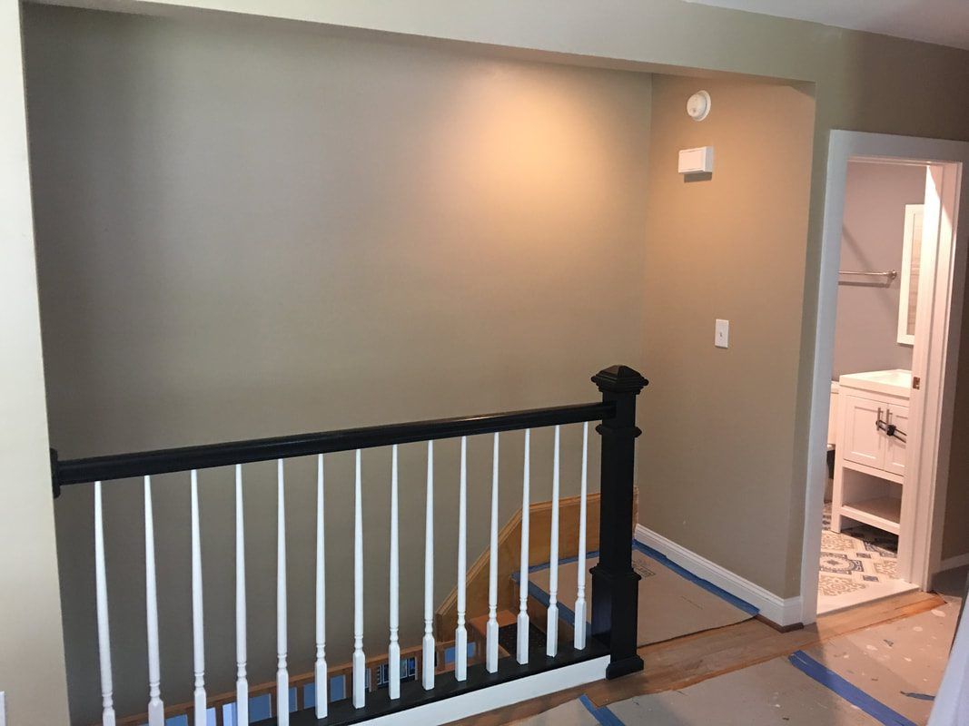 A hallway with a black and white railing, beige walls, and a view of a bathroom doorway.