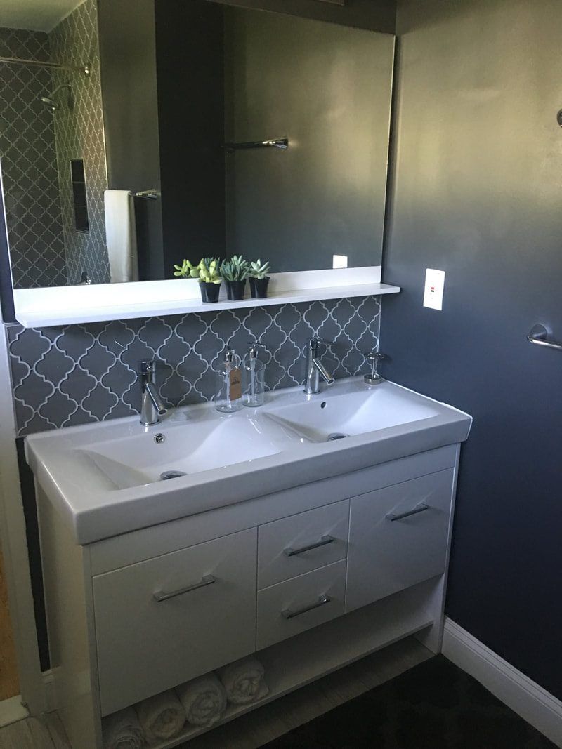 Modern bathroom with double sink vanity, dark walls, and decorative tile backsplash.