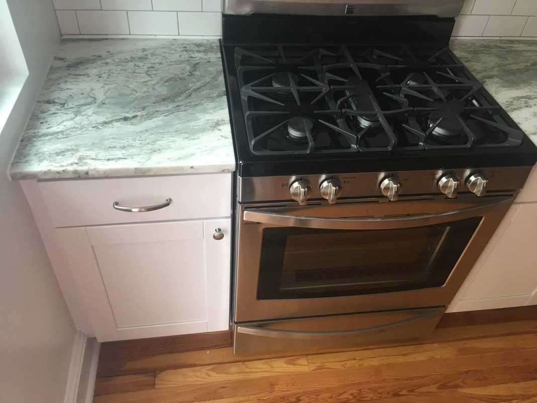 Stainless steel oven and gas stove next to a white cabinet with granite countertop.
