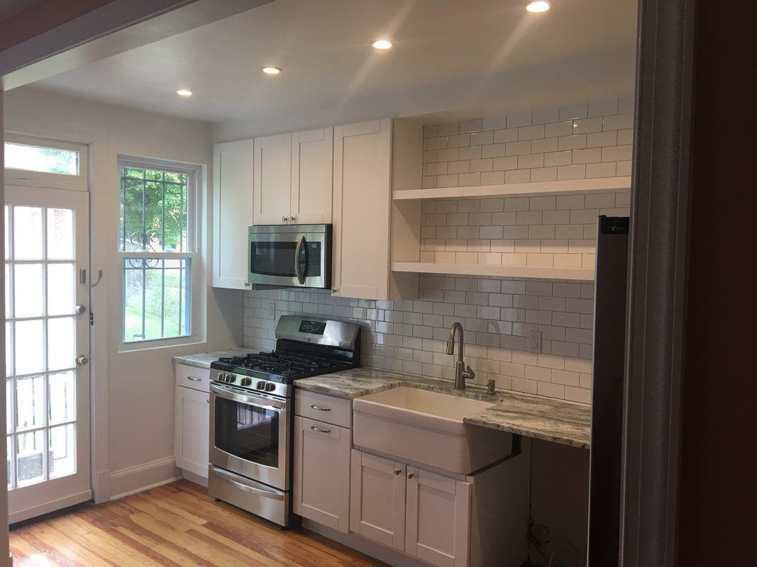 Accessible kitchen: white cabinets, stainless steel appliances, open shelves, apron-front sink, and hardwood floors.