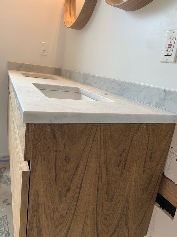 Wooden bathroom vanity with marble countertop and two rectangular sinks.