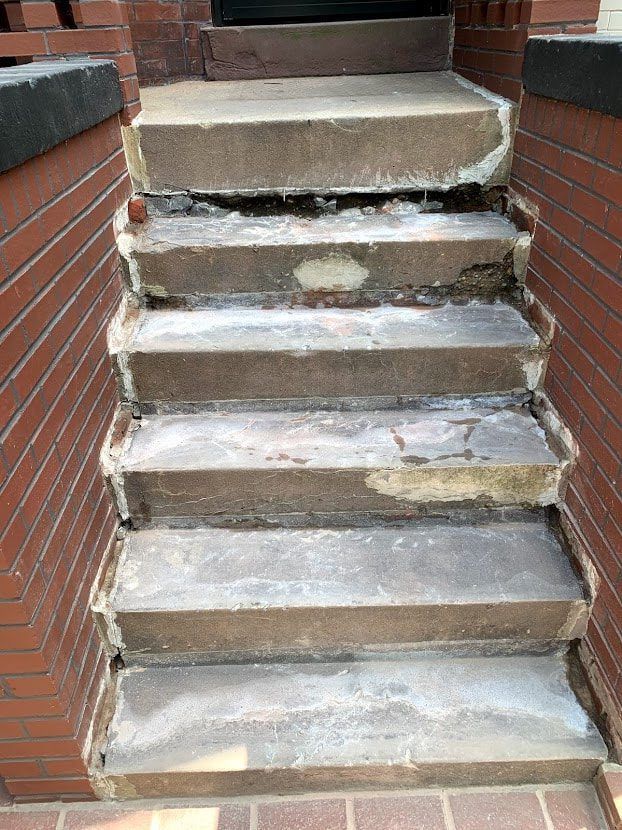 Concrete steps of a building show significant damage, with chipped edges and discoloration.