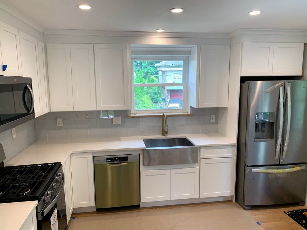 White kitchen with stainless steel appliances, farmhouse sink, and window.