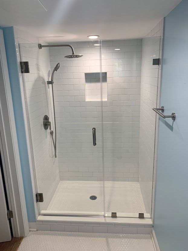 Glass shower enclosure with white subway tile, stainless steel fixtures, and a light blue wall.