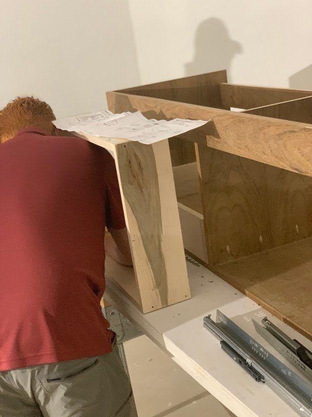 A person in a red shirt building a wooden structure in a room with white walls.