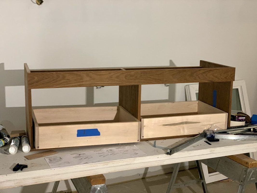 Wooden cabinet with two drawers, under construction, on a workbench in a garage.