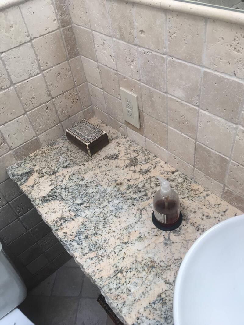 Bathroom counter with granite top, soap, and dispenser; beige tile backsplash and outlet.