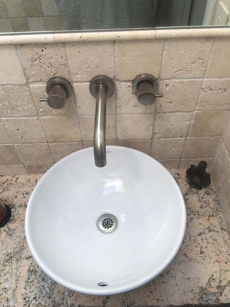 A white, round sink with a faucet and two handles, set into a stone countertop.